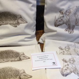 pile of chision coers in cream cotton with woodcut style print of rhino or hedgehog